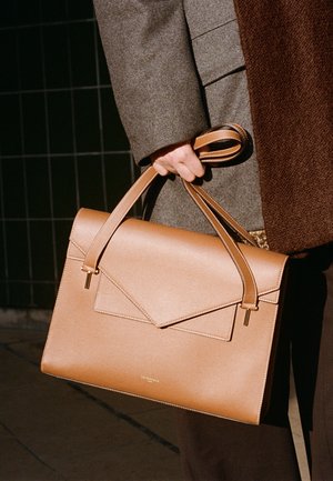 Borsa a mano in pelle tan con design strutturato, forma allungata e patta frontale. Presenta manici sottili e sottili accenti in hardware oro.