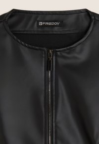 Giacca in ecopelle nera con colletto rotondo e zip argentata, con etichetta del marchio "FREDDY" visibile all'interno del colletto.