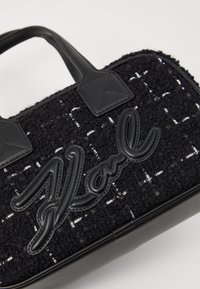 Μαύρη τσάντα χειρός με υφασμάτινο σώμα με υφή, δερμάτινες λεπτομέρειες και εμφανές �λογότυπο "Karl", που αναδεικνύει αντιθετικά υλικά και κομψό σχέδιο.