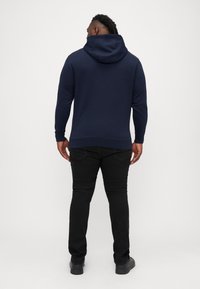 Granatowa bluza z kapturem z kieszenią kangurką, zestawiona z czarnymi jeansami slim-fit i czarnymi butami, widok z tyłu.