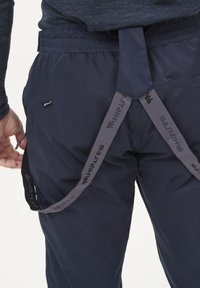Tummansiniset housut, joissa on säädettävä vyötärö ja harmaat henkselit, jotka ovat brändätty. Silkkinen kangas, rento leikkaus ja sivutaskut.