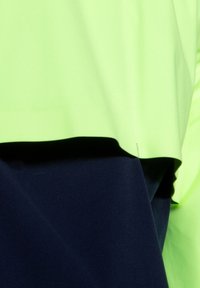 Haut vert néon à coupe ample tombant sur un bas bleu marine uni. Les matériaux semblent lisses et légers avec des bords nets.