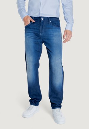 Jeans in denim con un gradiente blu, caratterizzati da un classico design a cinque tasche e chiusura con bottone. Indossati con una camicia a manica lunga azzurro chiaro.