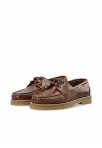 Braune Lederbootsschuhe mit weißen Nähten und goldenen Ösen. Texturierte Gummisohle für besseren Halt. Abgerundete Zehenpartie und niedrig geschnittenes Design.
