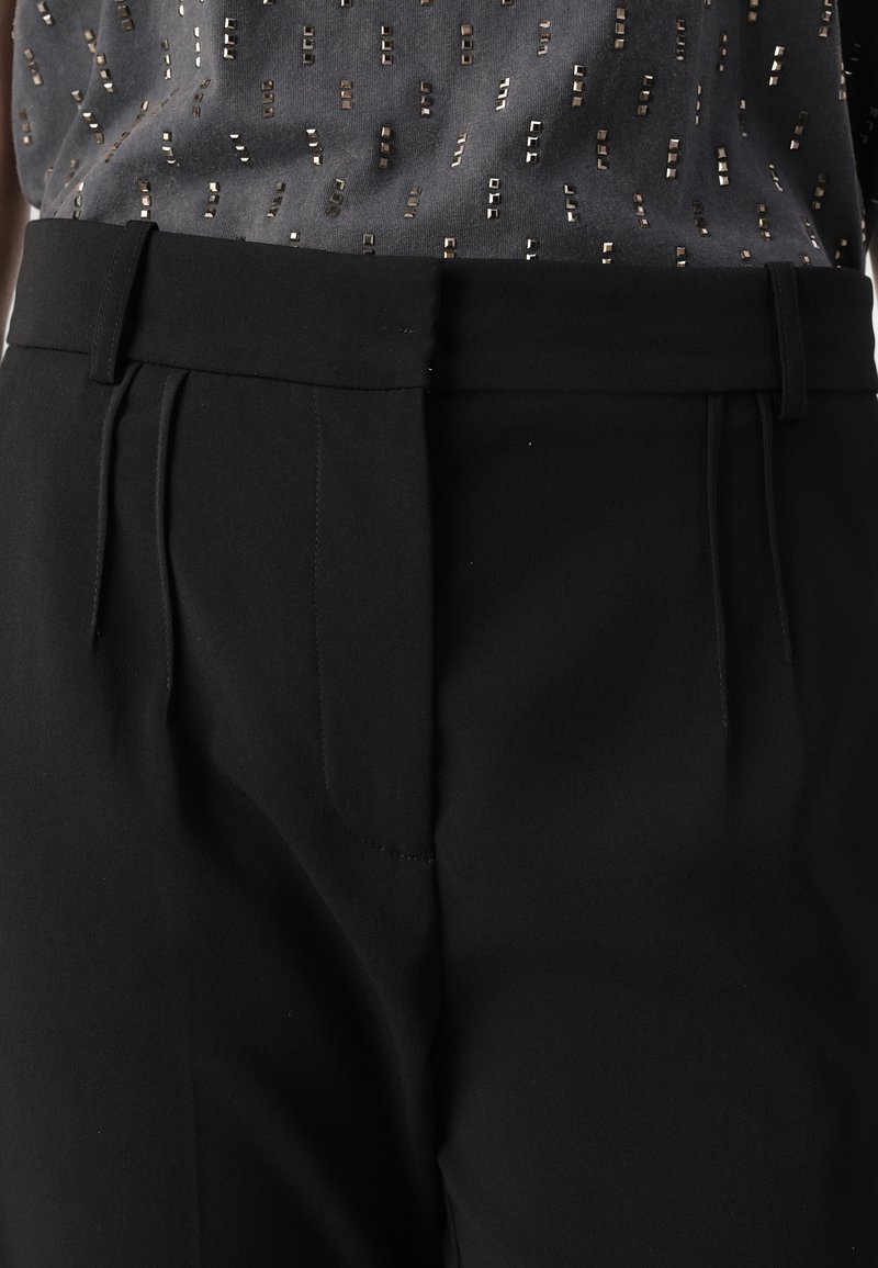 Czarne dopasowane spodnie z gładkim przodem, z bocznymi kieszeniami i gładką teksturą. Połączenie z szaro wzorzystą bluzką.