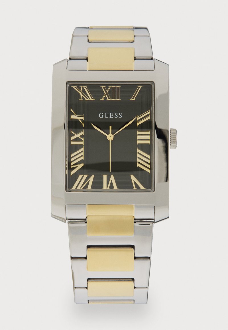 Négyzetes Guess karóra fekete számlappal és római számokkal, ezüst fém házzal, valamint ezüst és arany színű, két tónusú fém szíjjal.