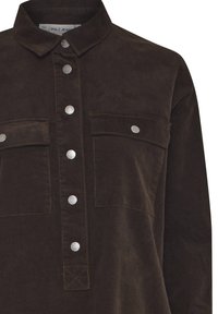Tamnosmeđa kordurova košulja s ovratnikom, prednjim kopčama na drukere i dva džepa na prsima s preklopom i kopčama na drukere.