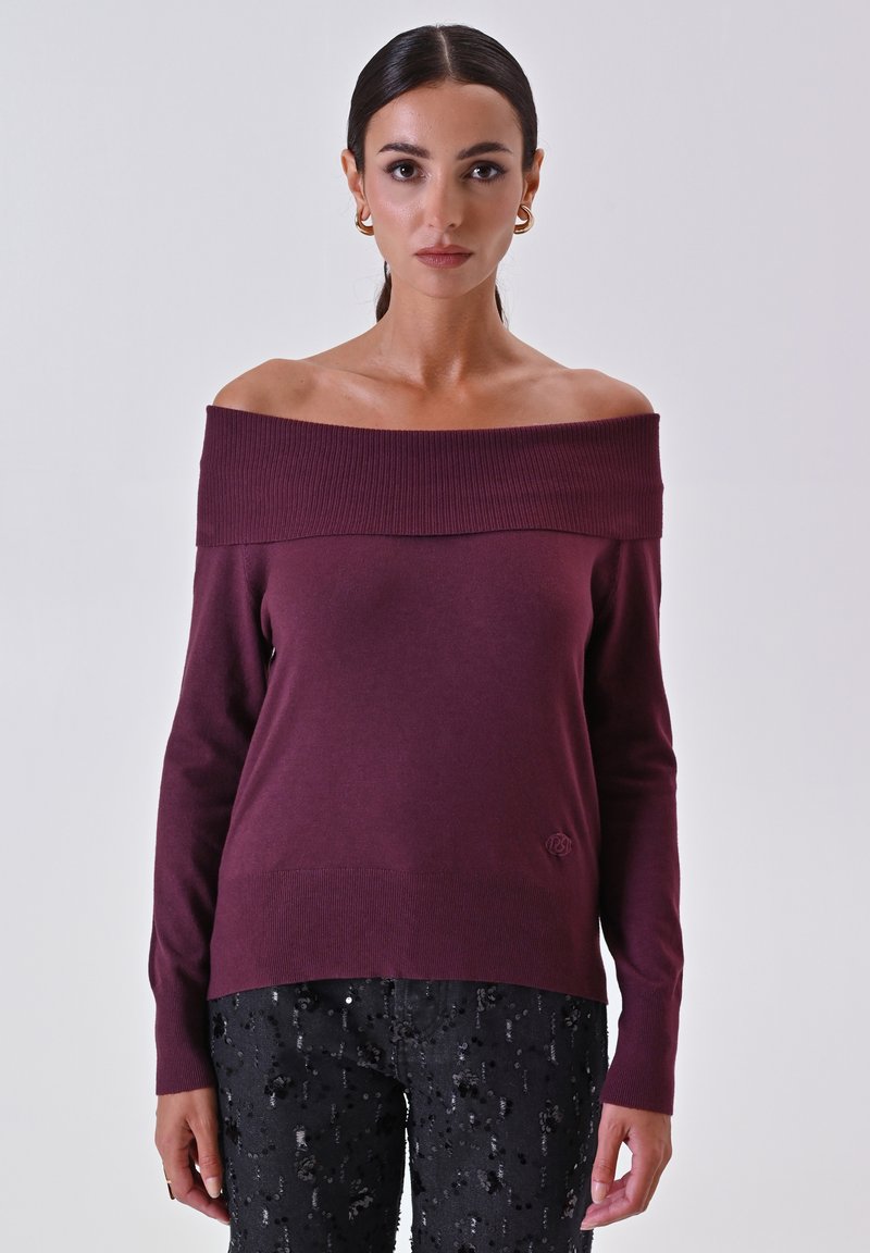 Bordeaux off-shoulder trui van zachte brei, met geribbelde halslijn en manchetten, gecombineerd met zwarte broeken met pailletten en een subtiel logo-detail.