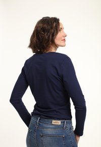 Granatowa bluzka z długim rękawem wykonana z bawełny, z okrągłym dekoltem, w połączeniu z niebieskimi dżinsami, pokazująca widok z tyłu.
