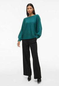 Pull à col rond en maille côtelée teal avec des manches larges, associé à un pantalon noir à jambes larges et des bottes à talons noirs pointues. Design simple et fluide.