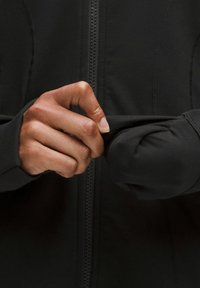 Čierna bunda so zipsom; priliehavé manžety s otvormi na palce; hladká textúra látky; ruka upravuje rukáv.