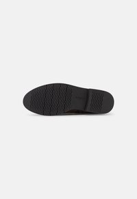 Suela de zapato de goma negra con un patrón texturizado, que presenta una banda de rodadura ondulada y un área de talón lisa. Nombre de la marca "Gabor" grabado en el lado.