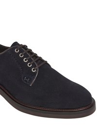 Pantofii de tip dress din suede bleu marin, cu vârf rotund, șireturi maro contrastante, detalii cusute și talpă plată, întunecată.