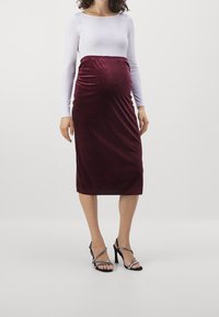 Mammaskjol i sammet i bordeaux med en figurnära design, elastisk midja och knälång längd. I kombination med svarta strappy högklackade sandaler.