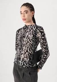 Black and cream long-sleeve top with an abstract animal print, paired with a black handbag. Textured fabric and fitted design.