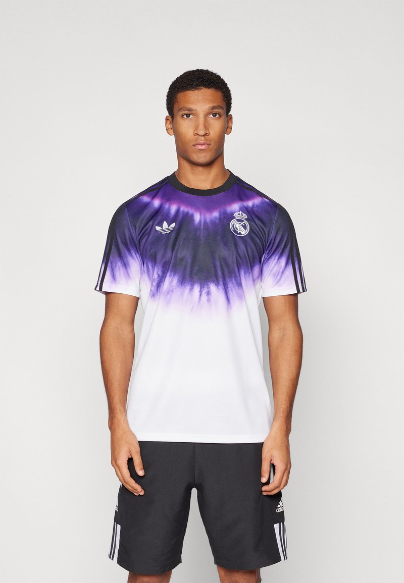 Lila-fehér átmenetes sportmez fekete részletekkel, az Adidas logóval és a Real Madrid címerével a mellkasán, rövid ujjal.