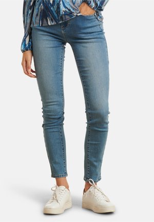Light blue skinny jeans made from denim, featuring a high waist, subtle fading, and stitched detailing at pockets paired with white sneakers.