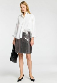 Hvid, langærmet skjorte med knaplukning parret med en metal sølvfarvet nederdel. En sort taske og spidse hæle fuldender outfittet.