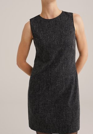 Vestido sin mangas, textura gris oscuro, largo hasta la rodilla, usado por una persona sobre un fondo liso beige.