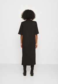 Schwarzes, schlichtes Kleid in mittellanger Form mit kurzen Ärmeln, aus einem glatten Material gefertigt. Es hat eine gerade Silhouette und ein minimalistisches Design.