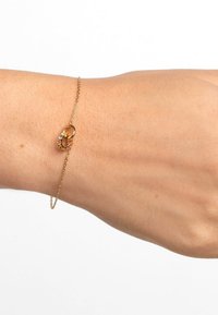 Bracciale in catena dorata con design a occhiello e un piccolo accento di pietra preziosa. La superficie testurizzata e i delicati link conferiscono un aspetto elegante.