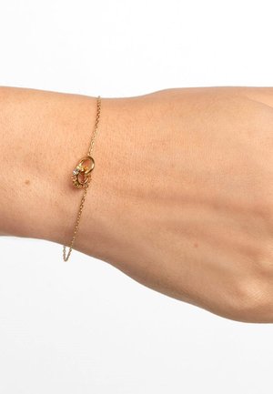 Bracciale in catena dorata con design a occhiello e un piccolo accento di pietra preziosa. La superficie testurizzata e i delicati link conferiscono un aspetto elegante.
