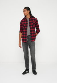 Rød- og svart rutete flanellskjorte, grå t-skjorte under, svarte jeans og svarte sneakers med hvite striper. Lang flette.