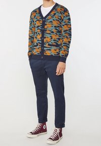 Kardigan med mörkblå bas, featuring en texturerad, flerfärgad palmträdsmönster i orange och teal. Knappstängning fram, ribbade ärmslut.