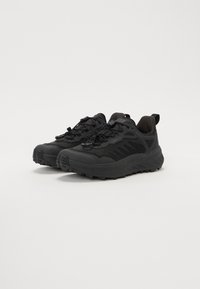 Chaussures de trail noires avec une tige en mesh et une semelle en caoutchouc, dotées d'un épais profil, d'un système de laçage flexible et d'une languette à l'arrière pour un enfilage facile.