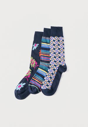Három színes tengerészkék zokni virágos, csíkos és kockás mintákkal, egymás mellett fehér háttéren elhelyezve.