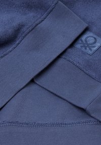 Capas de tela azul marino: textura suave y cepillada en la parte superior, parte inferior lisa con una costura, que presenta un parche con un logotipo y un símbolo.