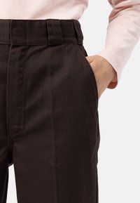 Hnědé bavlněné kalhoty s uvolněným střihem, pevný pas a boční kapsy, s hladkou texturou a čistými liniemi.