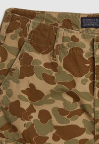Camo-patterned shorts in tan, green, and brown tones, with a textured fabric and reinforced stitching on pockets and waistband.