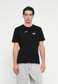 Μαύρο βαμβακερό T-shirt με κοντά μανίκια, που διαθέτει μπροστινό σχέδιο με λευκό γραφικό τύπωμα και μικρό λογότυπο στο στήθος.