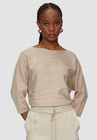 Beżowy sweter z rękawami 3/4, zdobiony białymi wzorami w paski. Miękka tekstura, okrągły dekolt, w połączeniu z jasnobeżowymi spodniami o elastycznym pasie.