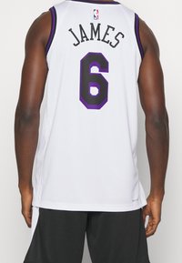Canotta da basket bianca con accenti viola, presenta 'JAMES' e il numero '6' in nero sul retro. Materiale leggero e traspirante.