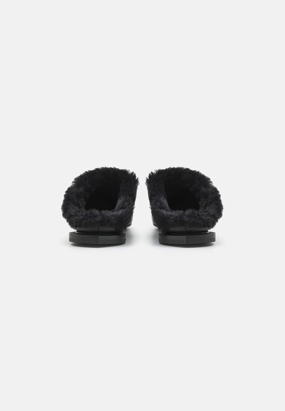Chaussons noirs à enfiler avec une doublure en fausse fourrure douce et une semelle noire texturée, présentant un design arrondi et ouvert à l'arrière.
