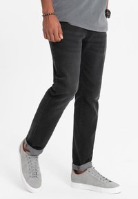 Jeans in denim nero con vestibilità dritta, con orli arrotolati. Abbinati a sneakers grigio chiaro, i jeans presentano lievi segni di usura e una consistenza liscia.