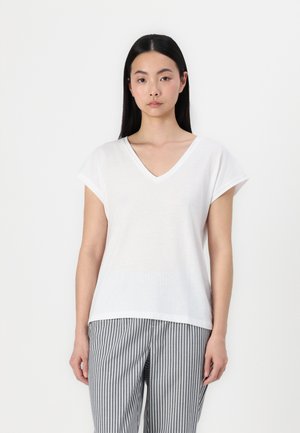 T-shirt blanche à col en V avec des manches courtes, texture douce, coupe décontractée, associée à un pantalon gris rayé. Design minimaliste, sans motifs ni accents.