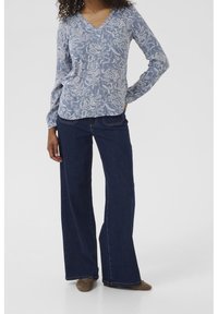 Blouse bleu clair à motifs avec un col en V et des manches longues, associée à un jean large bleu foncé et des chaussures plates marron.