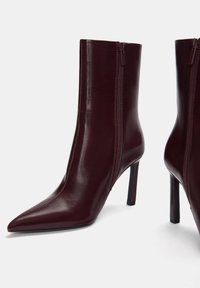 Burgunderrote Leder-Stiefeletten mit spitzem Zehenbereich, seitlichen Reißverschlüssen und 10 cm hohen Stiletto-Absätzen; glatte Textur mit glänzendem Finish.