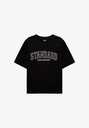 Zwarte katoenen t-shirt met een oversized pasvorm, korte mouwen, ronde halslijn, met de tekst "STANDARD CALM EVERYDAY" in witte en gemusterde letters gedrukt.