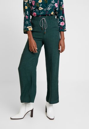 Groene linnenmix wijde broek met een elastische tailleband en trekkoord. Voorzien van zijsplitten. Gecombineerd met witte hoge laarzen.