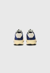 Blue sneakers with a textured fabric upper, cream accents, and a cushioned sole. Logo displayed on the heel. Clean, modern design.