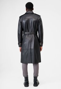 Black leather trench coat with a belted waist, shoulder epaulets, and a cinched back. Smooth texture with a straight silhouette.