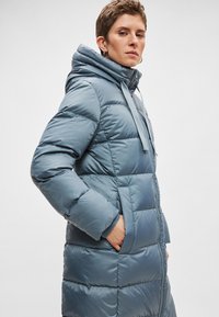 Gewatteerde blauwe jas met een hoge kraag en capuchon. Heeft een ritssluiting, zijzakken en een strak, glad stoffen oppervlak.