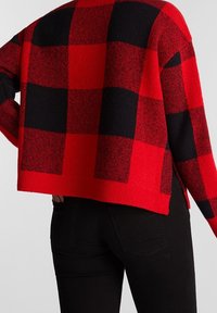 Suéter de cuadros rojo y negro con un diseño recortado, tejido texturizado y dobladillo acanalado. Presenta lados abiertos para un ajuste relajado.