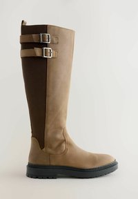 Knee-high pruunist nahast saapad elastsete paneelidega, kahe hõbedase pandlaga kaunistatud ja tekstuurse musta kummitaldaga, et tagada haarduvus.