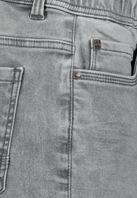 Grey denim jeans with a slightly faded texture, featuring a visible metal button, back pocket stitching, and a small branded tag.