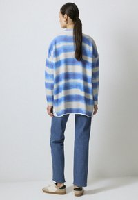 Oversized gebreide sweater met blauw en witte horizontale strepen, geribbelde textuur, gecombineerd met rechte spijkerbroeken en beige sneakers.